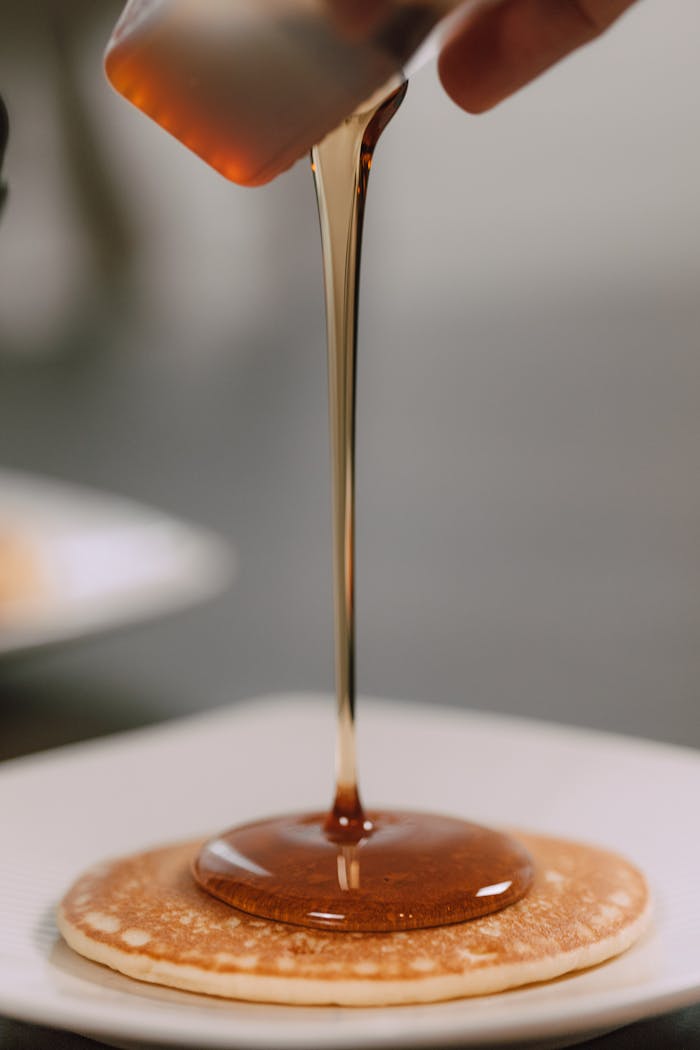 Close-up of a pancake topped with flowing maple syrup, captured indoors.